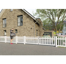 Weißer Gartenzaun vor einem Wohnhaus.