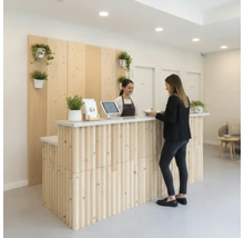 Empfangsbereich mit Holztheke, Pflanzen und zwei Personen.