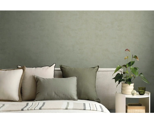 Modernes Schlafzimmer mit Kissen in Grün und Creme vor einer strukturierten olivgrünen Wand und einer Anthurium Pflanze.