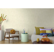 Wohnzimmer mit strukturierter Tapete, Holzarmsessel mit Knotenkissen, Beistelltisch und Sofa mit bunten Kissen auf Parkettboden.