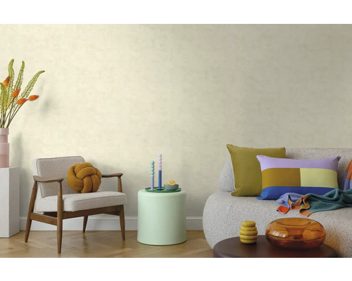 Wohnzimmer mit strukturierter Tapete, Holzarmsessel mit Knotenkissen, Beistelltisch und Sofa mit bunten Kissen auf Parkettboden.