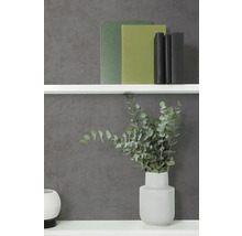 Vliestapete in Anthrazit mit Betonoptik und feiner Struktur, kombiniert mit einem weißen Regal, Büchern und einer Vase mit Eukalyptus.