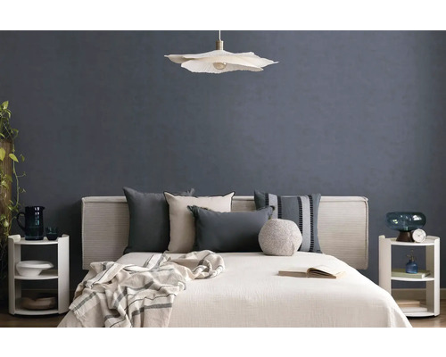 Modernes Schlafzimmer mit Bett, diversen Kissen, einer Pendelleuchte und Nachttischen vor einer strukturierten Wand.