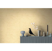 Strukturierte Tapete in warmem Gelb an einer Wand hinter einem Sideboard mit dekorativer Vogelfigur, Vase mit Baumwollzweig und Kerzenhaltern.