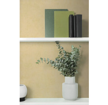 Strukturierte ockerfarbene Tapete in modernem Interieur mit weißen Regalen, Büchern und einer Vase mit Eukalyptus.
