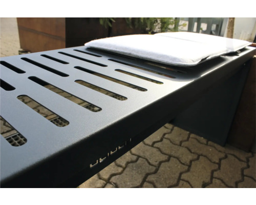 Detailansicht eines grauen Metallgrills mit Lüftungsschlitzen und weißem Kissen