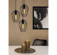 Drei schwarze Pendelleuchten mit Drahtschirmen über einem Esstisch mit Dekoration