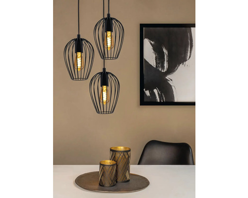 Drei schwarze Pendelleuchten mit Drahtschirmen über einem Esstisch mit Dekoration