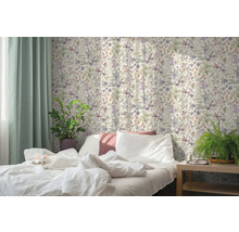 Helles Schlafzimmer mit einer Katze auf dem weißen Bett, Blumentapete im botanischen Stil, grünen Vorhängen und Zimmerpflanzen.