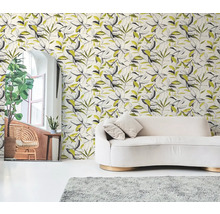 Vliestapete mit botanischem Blättermuster in Schwarz und Gelb hinter einem cremefarbenen Sofa in einem hellen Wohnzimmer.