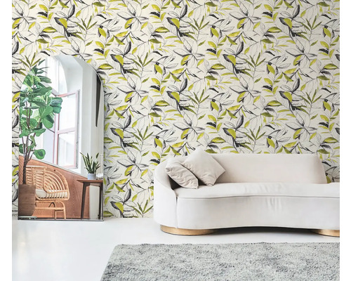 Vliestapete mit botanischem Blättermuster in Schwarz und Gelb hinter einem cremefarbenen Sofa in einem hellen Wohnzimmer.