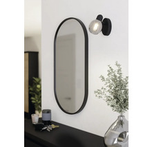 Ovaler Spiegel mit Lampe und Dekoration auf einer Kommode.