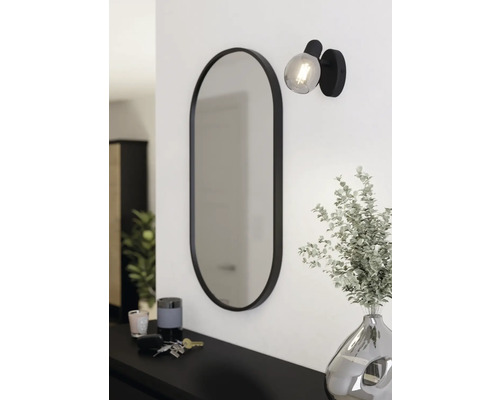 Ovaler Spiegel mit Lampe und Dekoration auf einer Kommode.