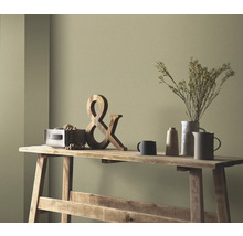 Dekorative Szene auf einem Holztisch mit Holzdekoration, Trockenblumen in einer Vase und Keramikgeschirr vor einer farbigen Wand.