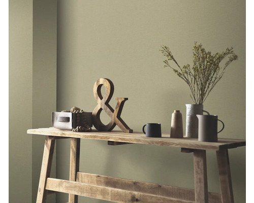 Dekorative Szene auf einem Holztisch mit Holzdekoration, Trockenblumen in einer Vase und Keramikgeschirr vor einer farbigen Wand.