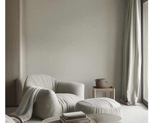 Wohnzimmer mit Sessel, Hocker, Beistelltisch und Vorhängen für eine helle und einladende Atmosphäre.