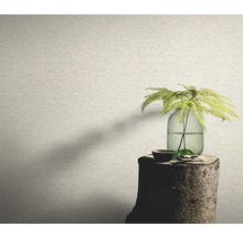 Nahaufnahme einer Wand mit einer Tapete in Steinoptik, auf einem Baumstumpf steht eine Vase mit einer Pflanze.