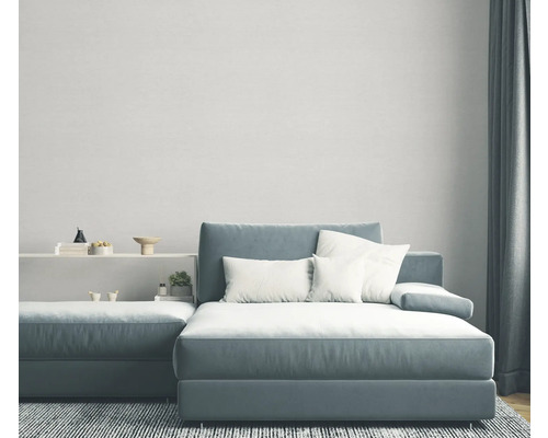 Wohnzimmer mit graublauem Ecksofa, weißen Kissen und grauem Teppich