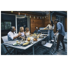 Gruppe von Personen isst und trinkt an einem Holztisch im Freien unter einer Lichterkette.