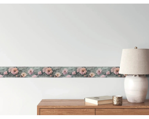 Tapetenborte mit rosa Blumenmuster an einer Wand über einer Holzkommode mit einer Tischleuchte.