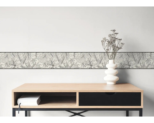 Wandbordüre mit schwarz-weißem botanischem Blättermuster auf einer hellen Wand über einem modernen Holzschreibtisch.