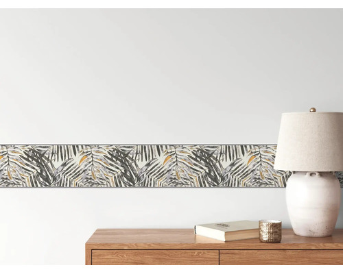 Helle und organisierte Raumszene mit einer Tapetenbordüre im Palmenblatt-Design an der Wand über einem Sideboard aus Holz mit einer Tischleuchte.