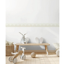 Helles Kinderzimmer mit Tapetenbordüre im Wellendesign an der Wand. Holzbank, Laufrad aus Holz und Weidenkorb auf hellem Holzboden.