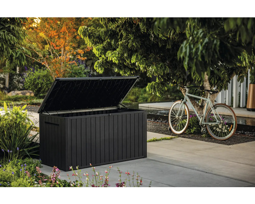 Geöffnete, dunkle Gartentruhe neben einem Fahrrad im Außenbereich.