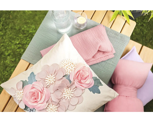 Dekorative Kissen und Textilien auf einer Holzbank im Garten.