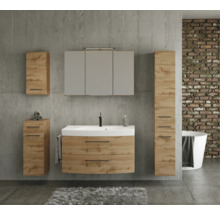 Modernes Badmöbel-Set in Eichenoptik mit weißem Waschtisch, Spiegelschrank, Hochschrank und Beistellschränken vor einer Betonwand.