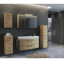 Modernes Badezimmerset in Eichenoptik mit Waschtischunterschrank, Spiegelschrank und Hochschränken vor dunkelgrauer Wand.