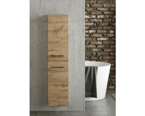 Badezimmer-Hochschrank in Eichenoptik mit schwarzen Griffen an einer Betonwand. Im Hintergrund eine Ziegelwand und eine freistehende Badewanne.