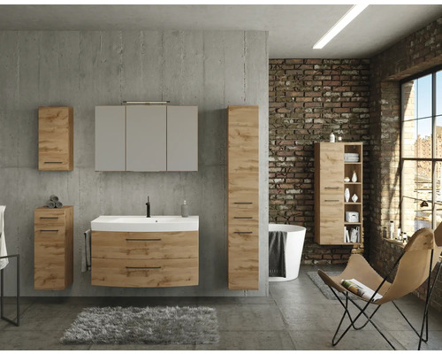 Modernes Badezimmer im Industrial-Stil mit Badmöbelset in Eichenoptik, Waschbeckenunterschrank, Spiegelschrank und Hochschränken vor Betonwand.