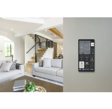 An der Wand montiertes Smart Home Bedienpanel in einem hellen, modernen Wohnzimmer mit Sofa und Treppe.