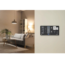 Smart Home Wanddisplay zur Steuerung von Beleuchtung und Temperatur in einem modern eingerichteten Wohnzimmer mit Sofa und Lampen.