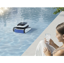 Ein Schwimmbad mit einem Poolreinigungsroboter im Wasser und einer Frau mit einem Glas Wasser am Beckenrand.