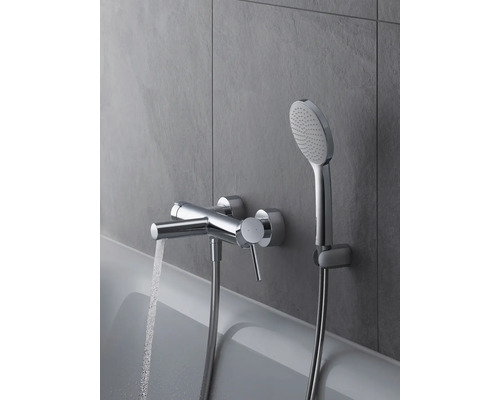 Aufnahme einer verchromten Badewannenarmatur mit Duschkopf an einer grauen Wand, Wasser läuft aus dem Wasserhahn.