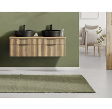 Moderner Waschtischunterschrank in Holzoptik mit Lamellenfront, zwei schwarzen Aufsatzbecken und Armaturen vor einer grünen Wand.