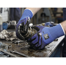 Eine Person hält eine ölige mechanische Komponente mit Arbeitshandschuhen.