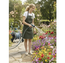 Eine Frau bewässert Blumen mit einem Gartenschlauch in einem üppigen Garten mit Rosenbogen