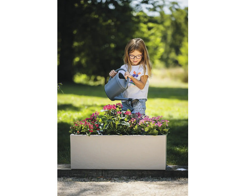 Mädchen gießt Blumen in einem rechteckigen Pflanzkasten im Garten.