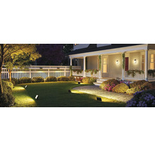 Beleuchteter Garten mit Haus, Rasen, Zaun und Strauchbepflanzung bei Nacht