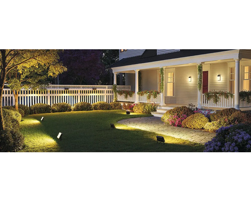 Beleuchteter Garten mit Haus, Rasen, Zaun und Strauchbepflanzung bei Nacht