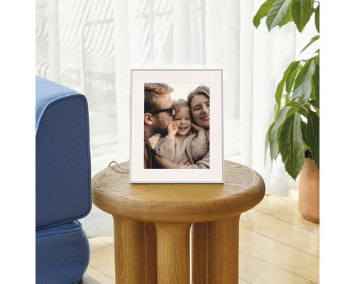 Digitaler Bilderrahmen auf einem runden Holzbeistelltisch im Wohnzimmer, zeigt ein Familienfoto