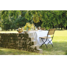 Gedeckte Gartentafel mit Mauer und Klappstuhl auf Rasen