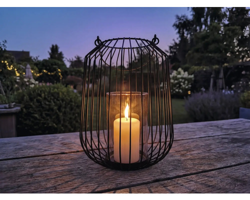 Dekorative Laterne aus Metall mit Glaseinsatz und brennender Kerze auf Holztisch