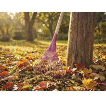 Gartenrechen aus Metall mit Holzstiel neben Baumstamm im Garten