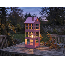 Dekorative Laterne in Hausform mit Kerze auf Holztisch im Garten