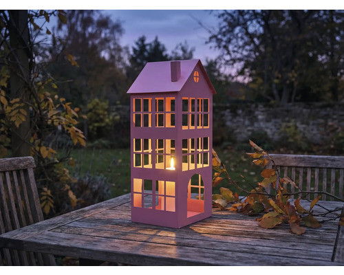 Dekorative Laterne in Hausform mit Kerze auf Holztisch im Garten