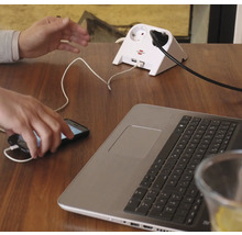 Steckdosenadapter mit USB Anschlüssen auf einem Tisch mit Laptop und Handy